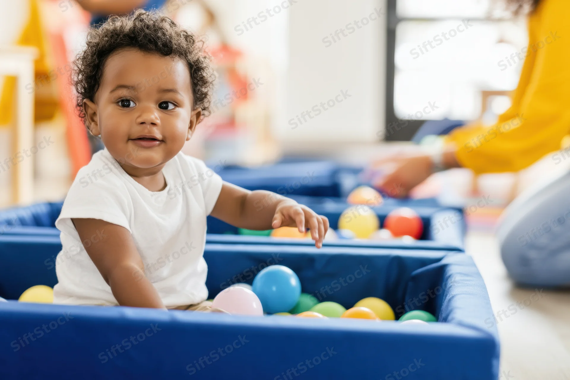 Smiling baby in white shirt playing in blue ball pit indoors