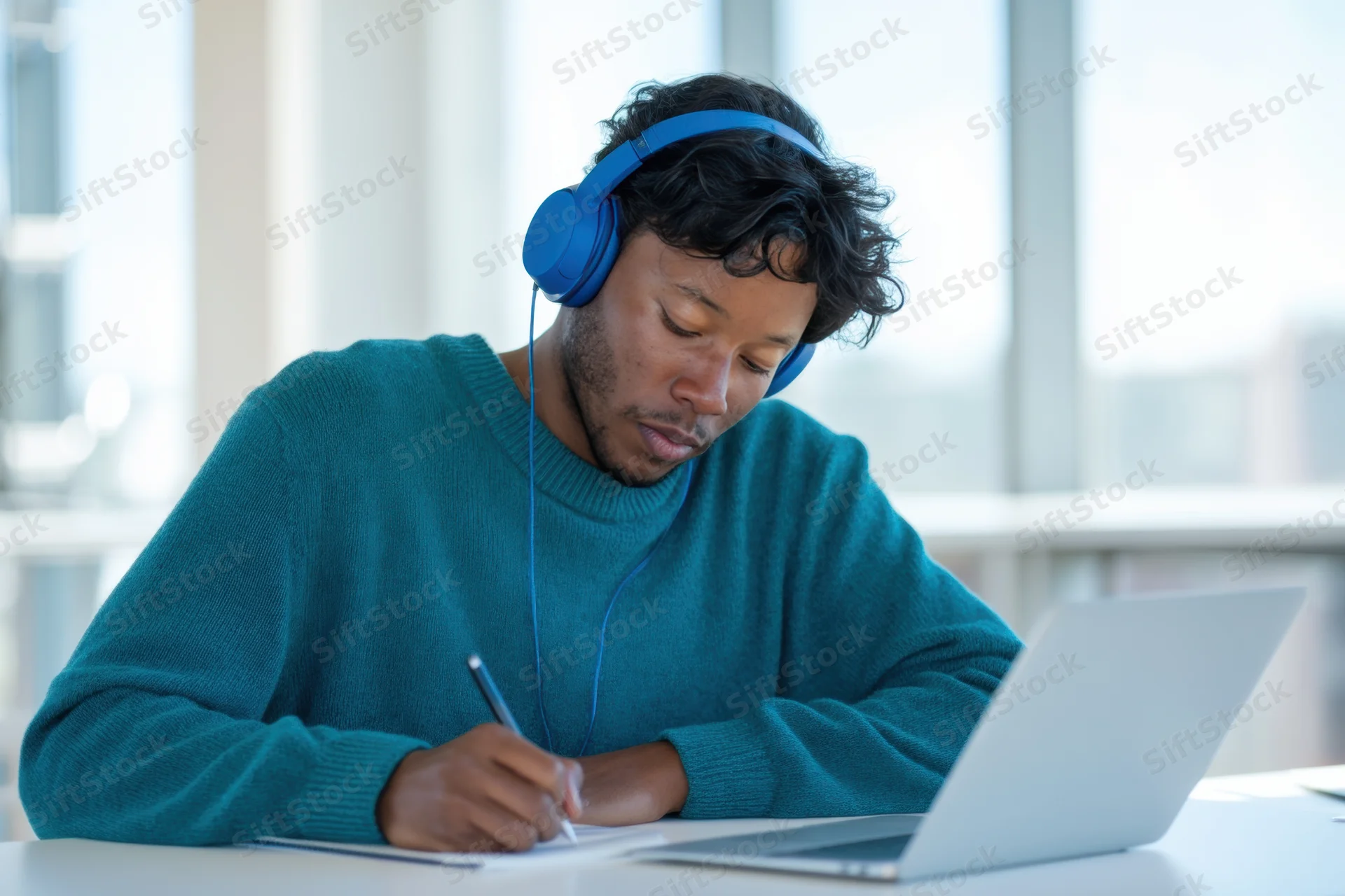 Young black man concentrating while studying with laptop and blue headphones at desk
