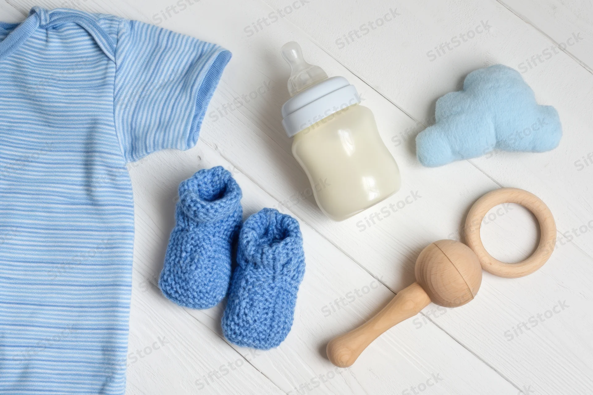 Baby essentials including clothing, bottle, socks, and toys arranged on white wooden surface