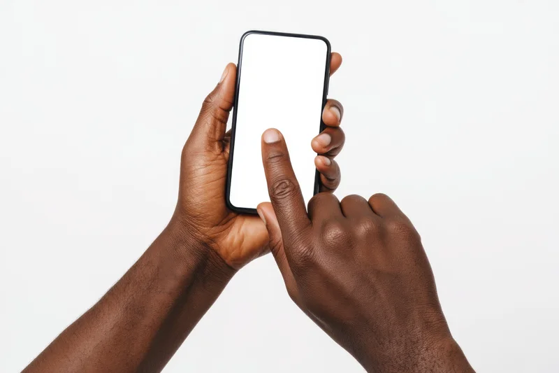 Dark-skinned hands holding and touching a smartphone with a blank white screen against a plain background
