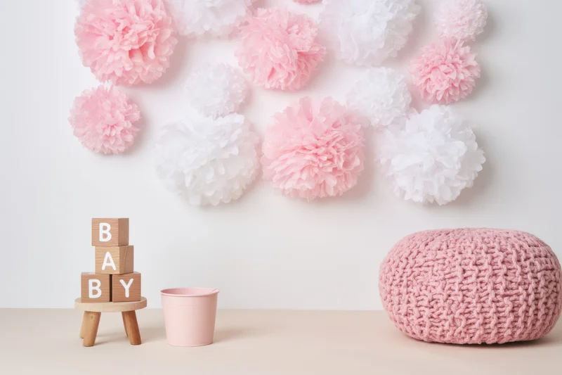Baby blocks spelling baby stacked on wooden stand beside pink bucket and knit pouf in pastel nursery decor