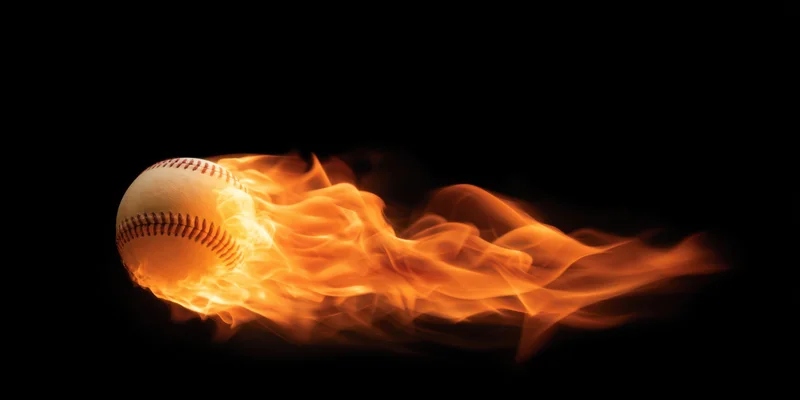 Baseball engulfed in bright orange flames streaking across black background