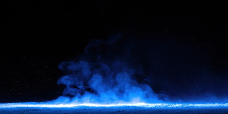 Wispy blue smoke rising above a glowing horizontal light strip in a dark space