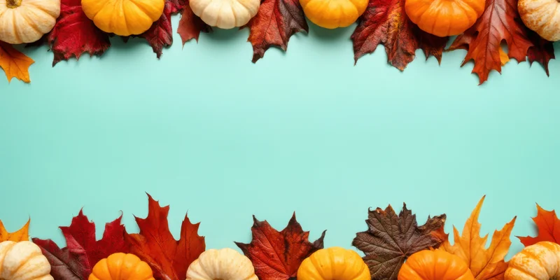 Small pumpkins and autumn leaves arranged in a border frame on a teal background with copyspace