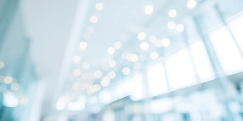 Blurred modern office interior with bright white walls and ceiling lights creating bokeh effect