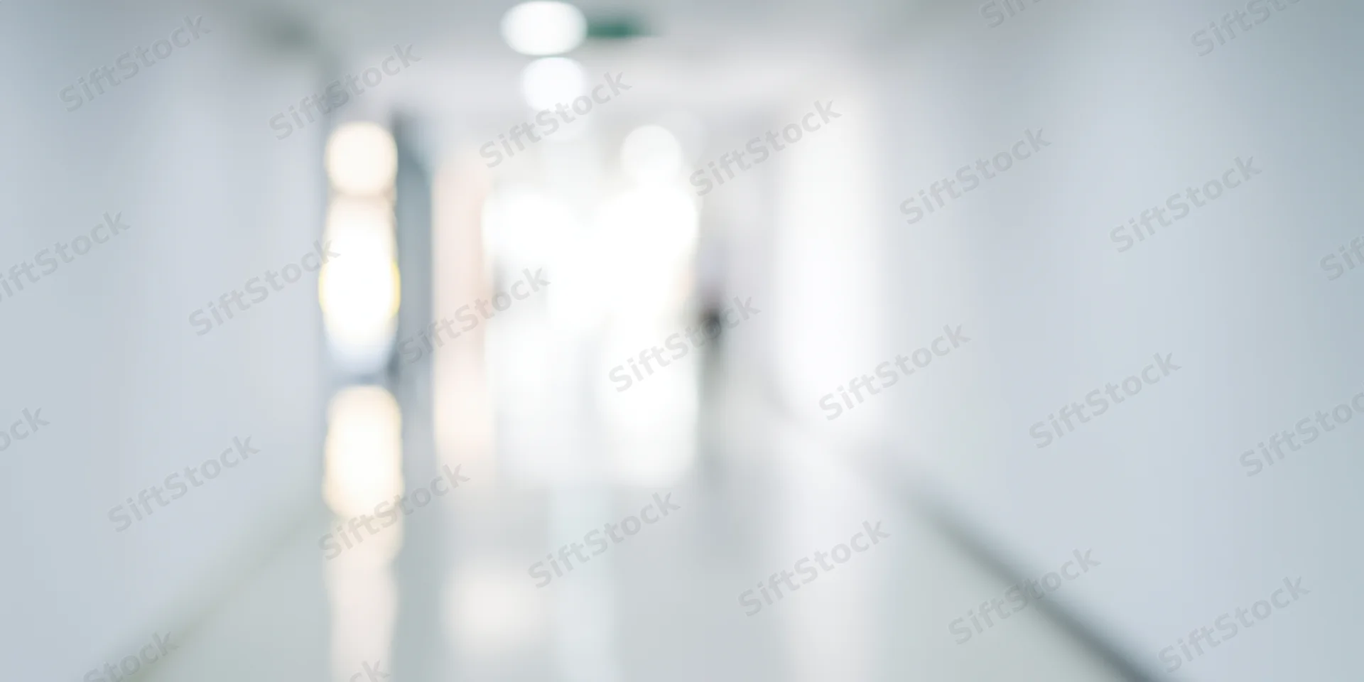 Blurred hallway with white walls and glossy floor reflecting ceiling lights