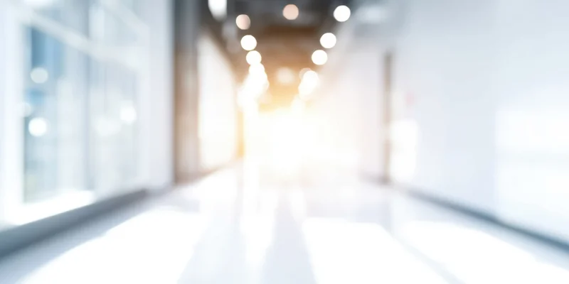 Blurred hallway with white walls and glossy floor leading into bright light