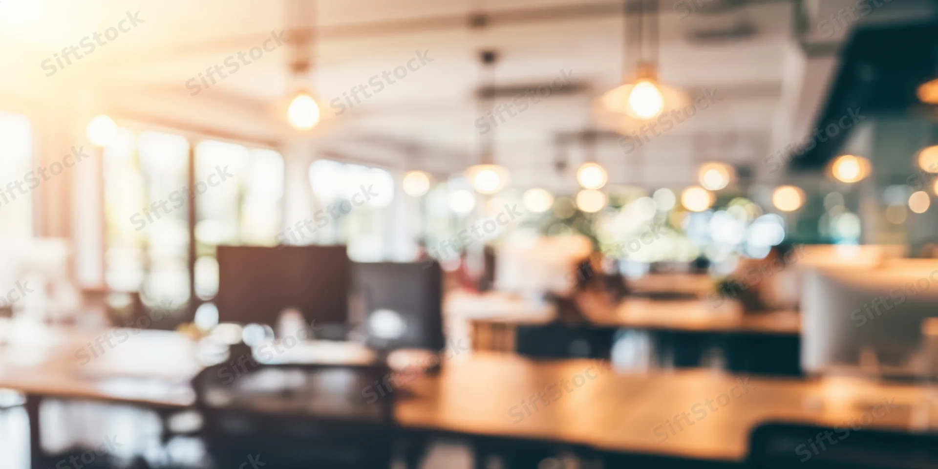 Blurred open-plan office interior with wooden desks and computer monitors under warm pendant lighting