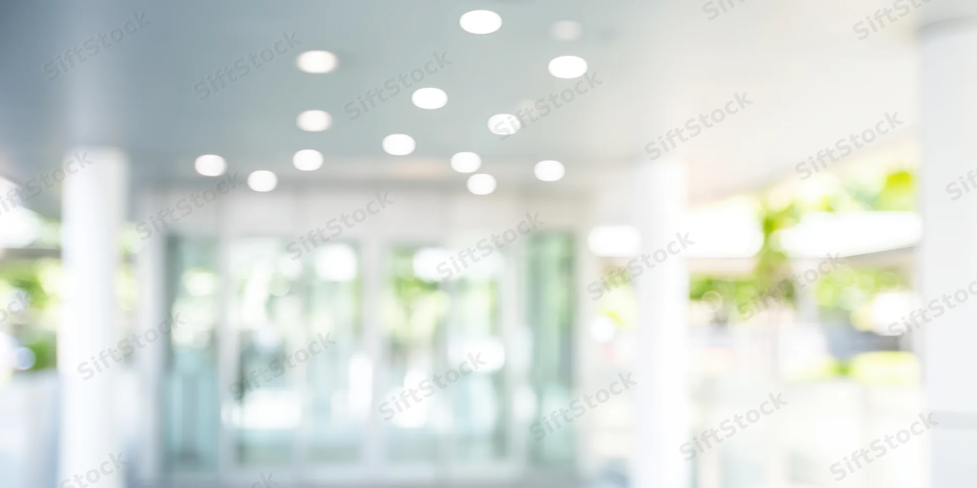 Bright out-of-focus entrance to a modern glass building with white columns and ceiling lights