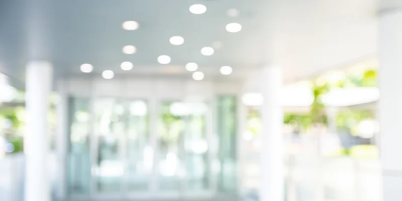 Bright out-of-focus entrance to a modern glass building with white columns and ceiling lights
