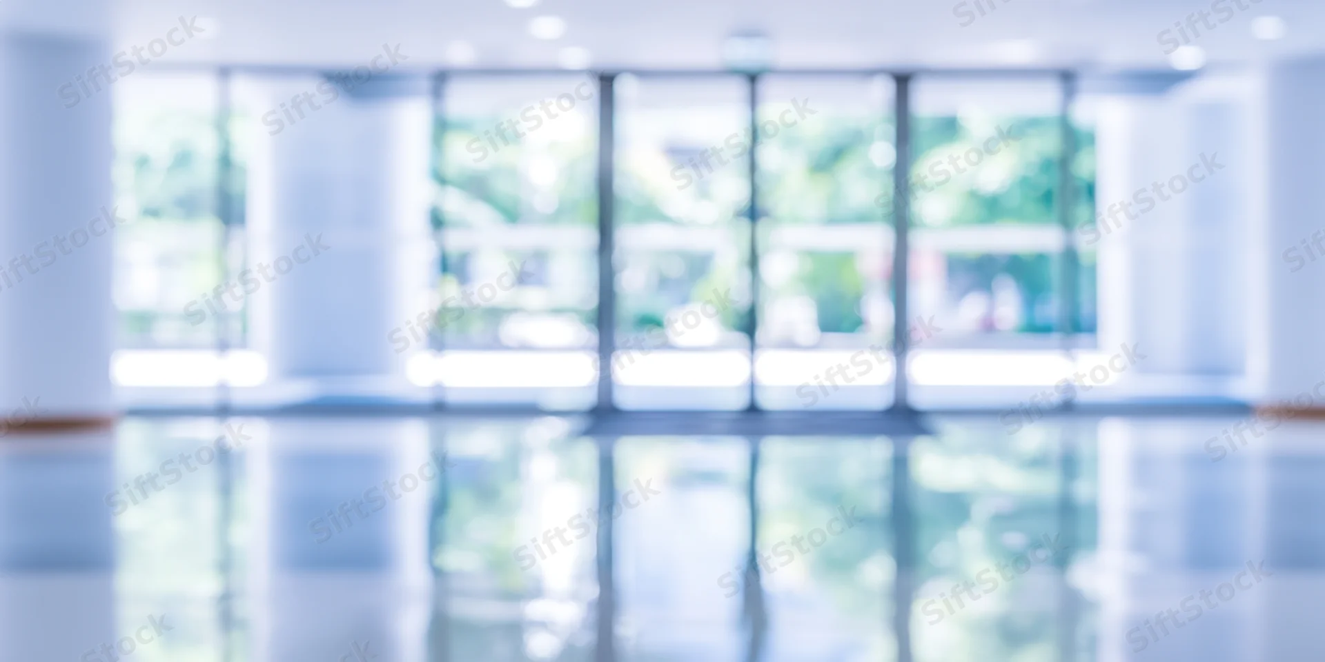Blurred entrance to modern building lobby with glass doors and reflective floor showing outdoor greenery