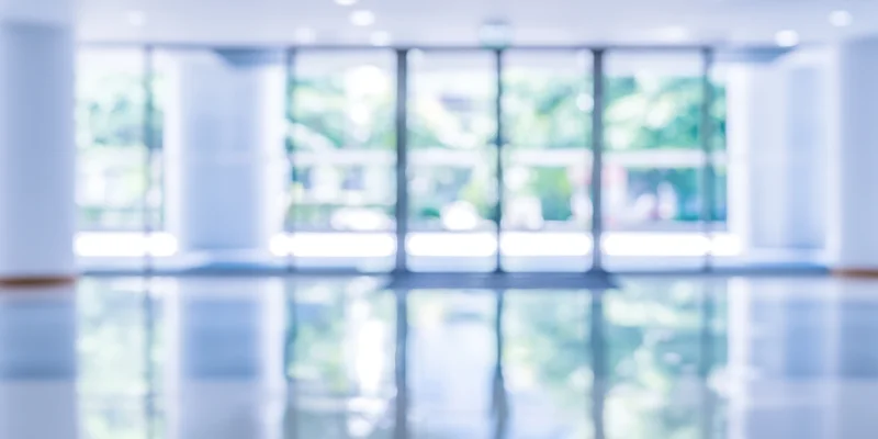 Blurred entrance to modern building lobby with glass doors and reflective floor showing outdoor greenery