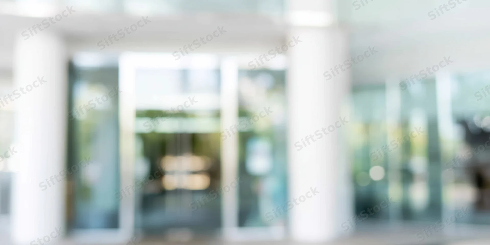Blurred entrance to a modern glass building with white columns and bokeh lighting
