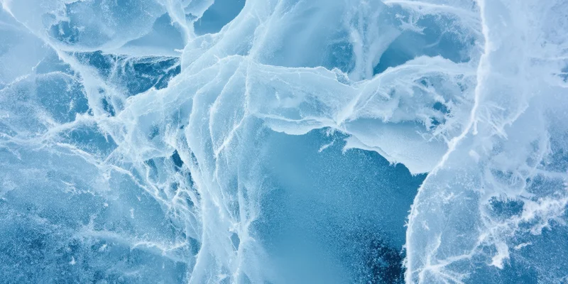 Close-up of blue ice with white cracks and frost patterns across its surface
