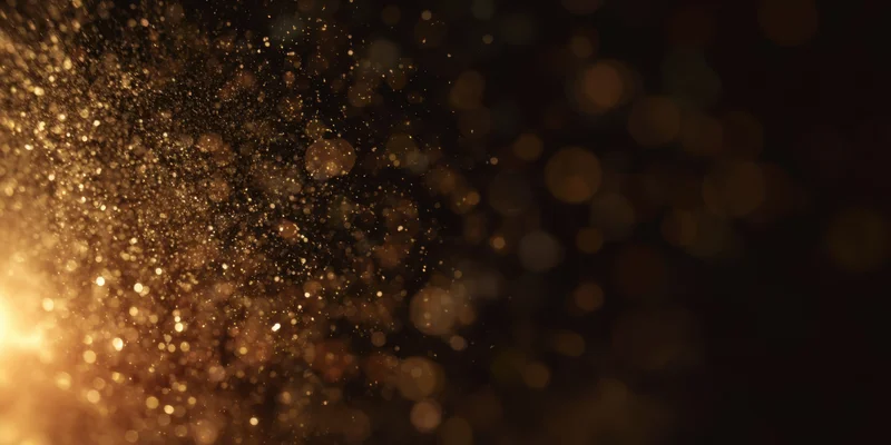 Golden dust particles floating in soft bokeh light against dark background