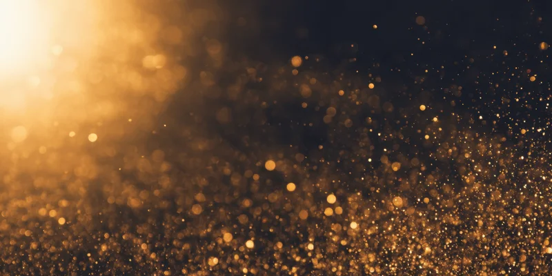 Golden dust particles floating in soft bokeh light against dark background
