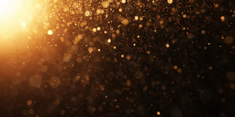 Golden dust particles floating in soft bokeh light against dark background