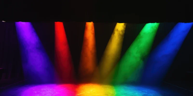 Six colored spotlights projecting rainbow beams through haze on a dark stage