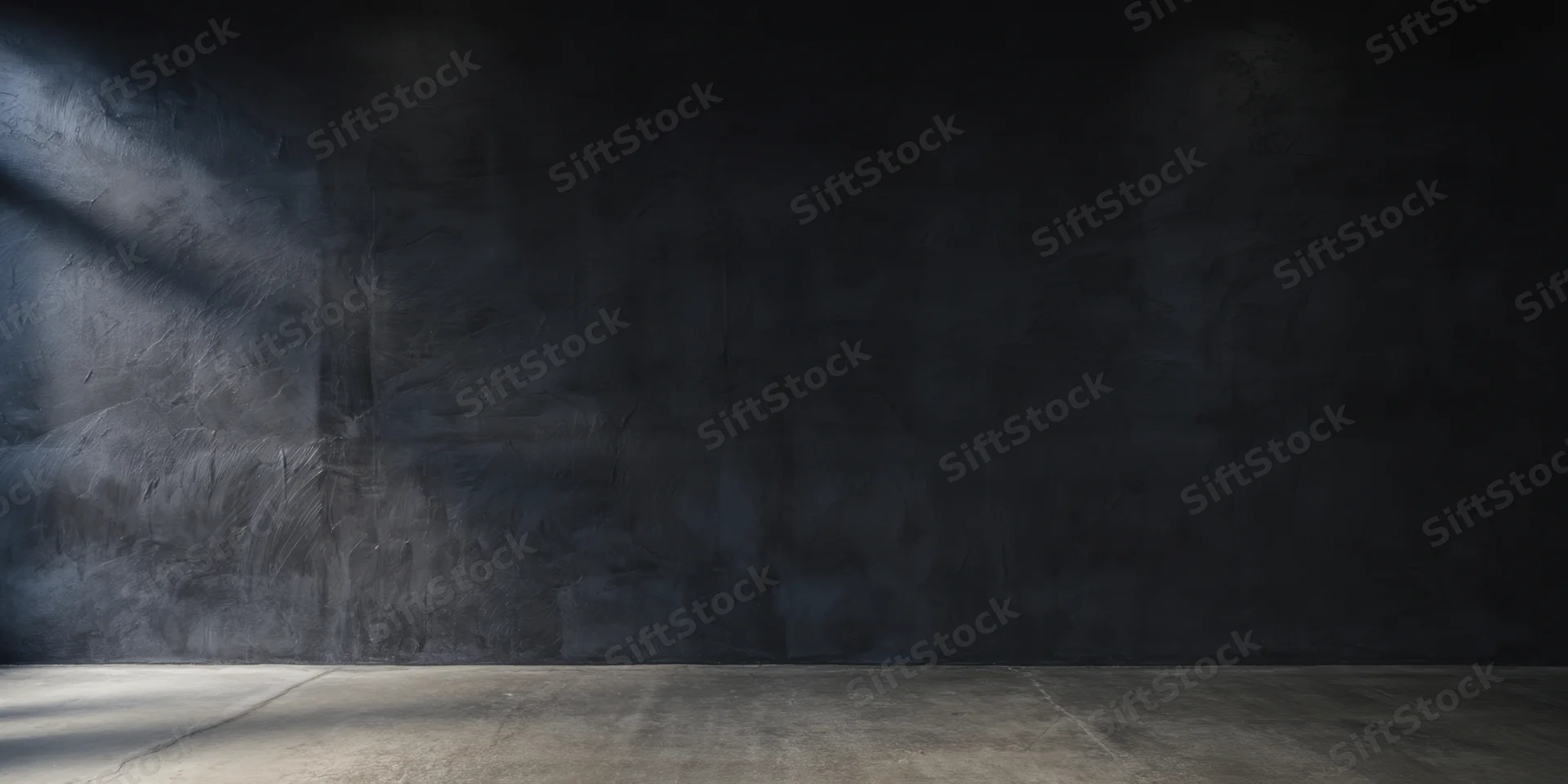 Dimly lit empty studio with rough charcoal-black textured wall and concrete floor