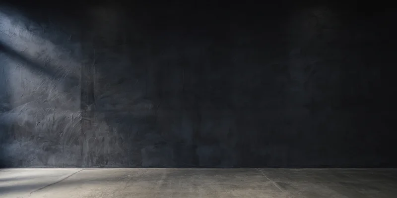 Dimly lit empty studio with rough charcoal-black textured wall and concrete floor