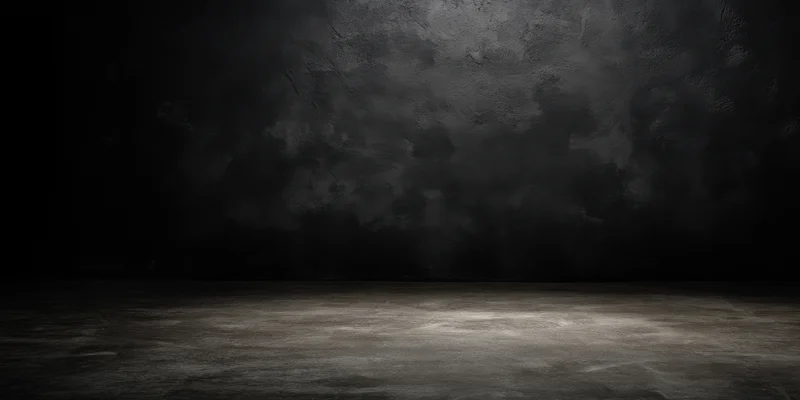 Dimly lit empty studio with rough charcoal-black textured walls and floor, spotlighted center copyspace