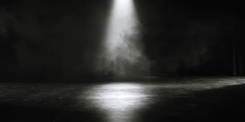 Single spotlight illuminating empty stage floor in black and white theater setting