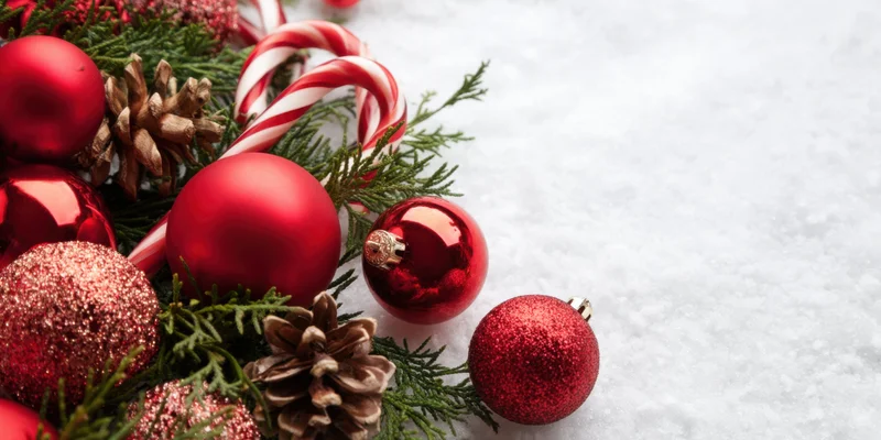 Red christmas ornaments and candy canes arranged with pine branches and pinecones on snowy surface