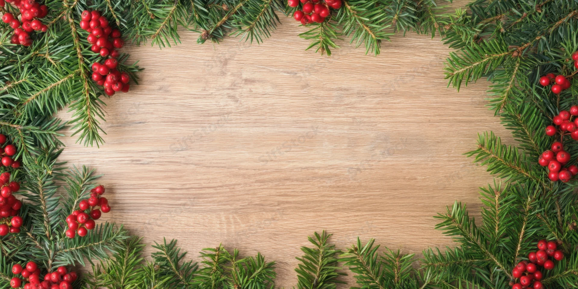 Evergreen branches with red berries arranged in a frame on a wooden surface