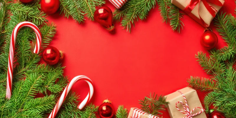 Evergreen branches and holiday decorations arranged in a border around a red background with copyspace