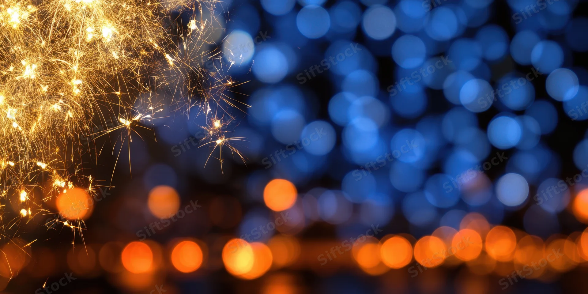 Golden fireworks sparks glowing against a blurred blue and orange bokeh background at night
