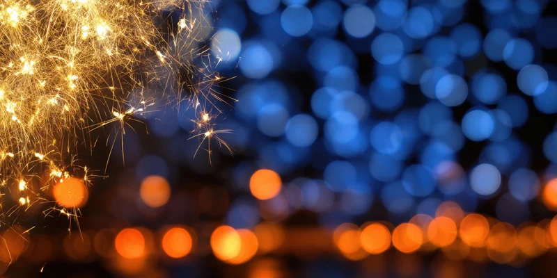 Golden fireworks sparks glowing against a blurred blue and orange bokeh background at night