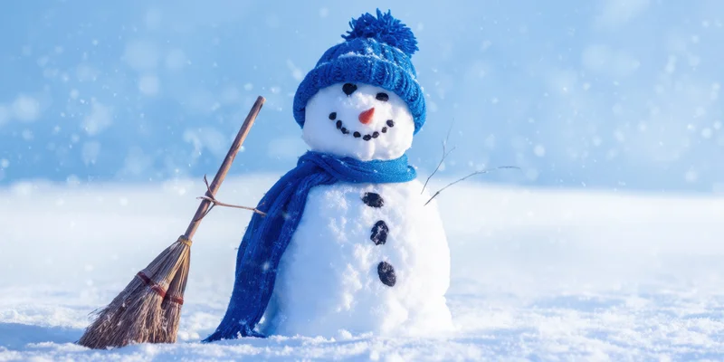 Cheerful snowman wearing blue knit hat and scarf standing in snow with broomstick beside it