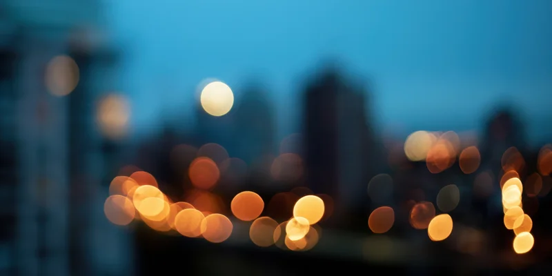 Blurred city lights at night with soft bokeh glow against a hazy sky