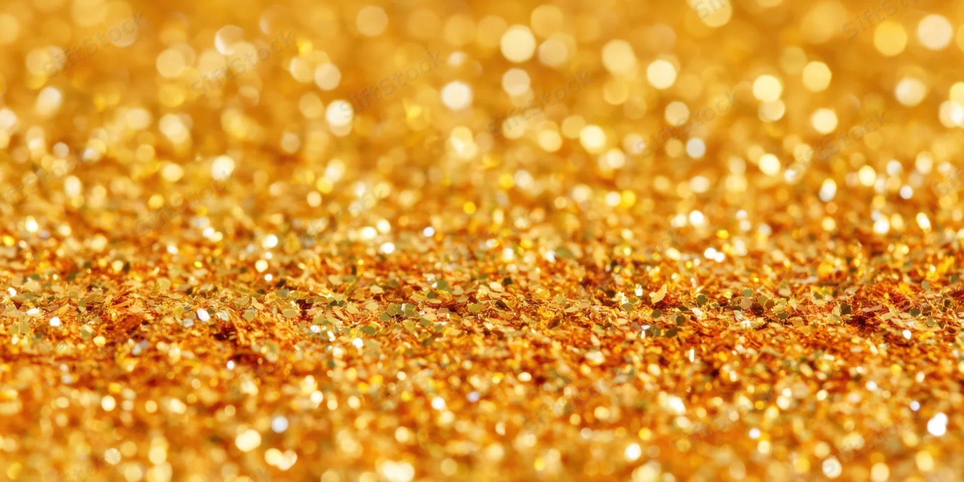 Gold glitter particles scattered across a surface in macro view with bokeh background