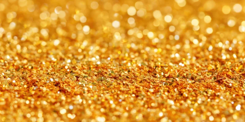 Gold glitter particles scattered across a surface in macro view with bokeh background
