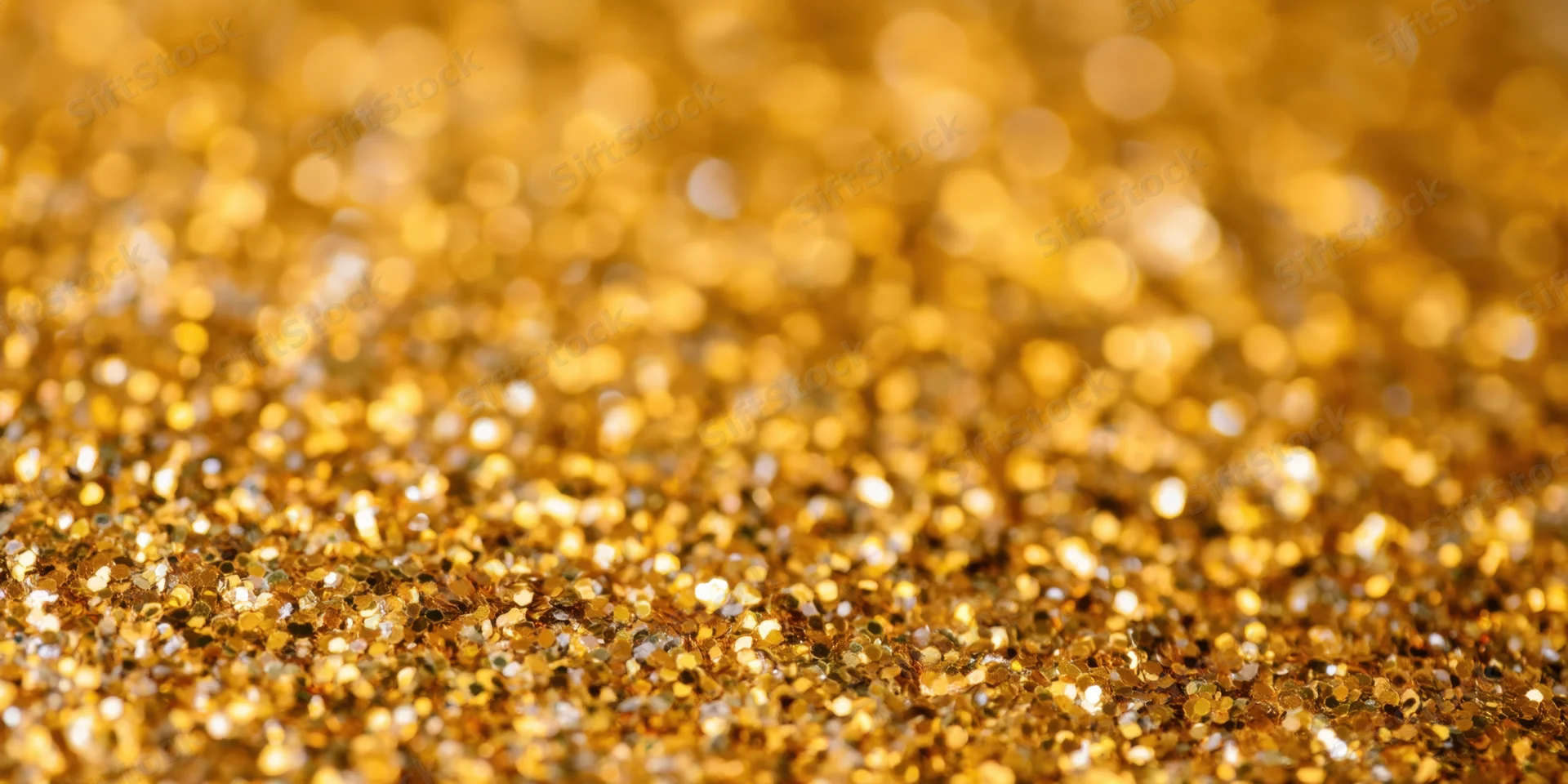 Gold glitter particles scattered across a surface in a macro closeup with bokeh background