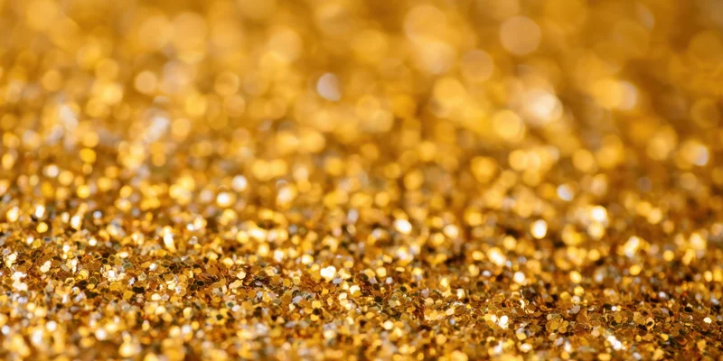 Gold glitter particles scattered across a surface in a macro closeup with bokeh background