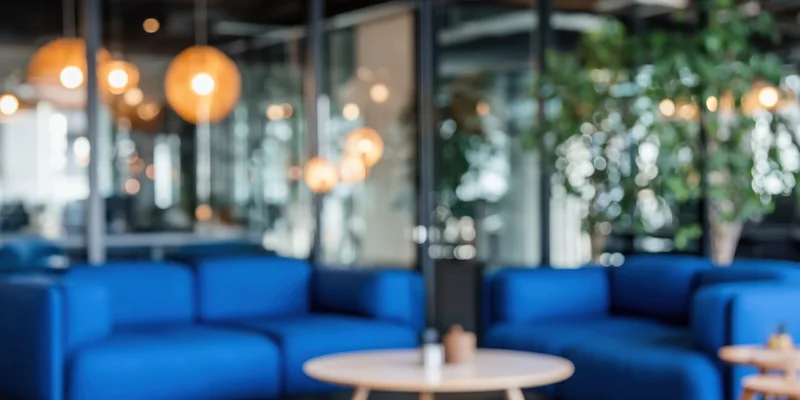Blue sofas and round wooden coffee table in modern office lounge with pendant lights and glass partitions