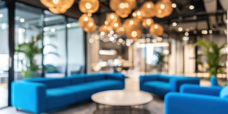Modern office lounge with blue sofas and round coffee table arranged around a central seating area with pendant lighting and glass partitions