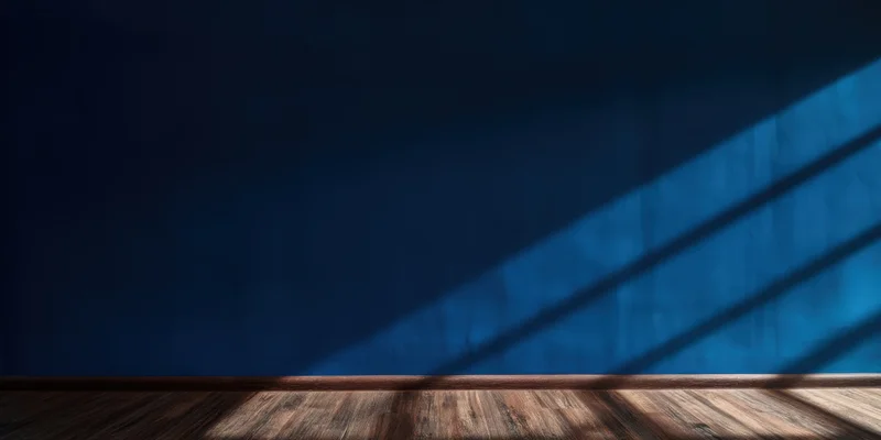 Empty room with deep blue wall and wooden floor lit by diagonal sunlight casting shadows