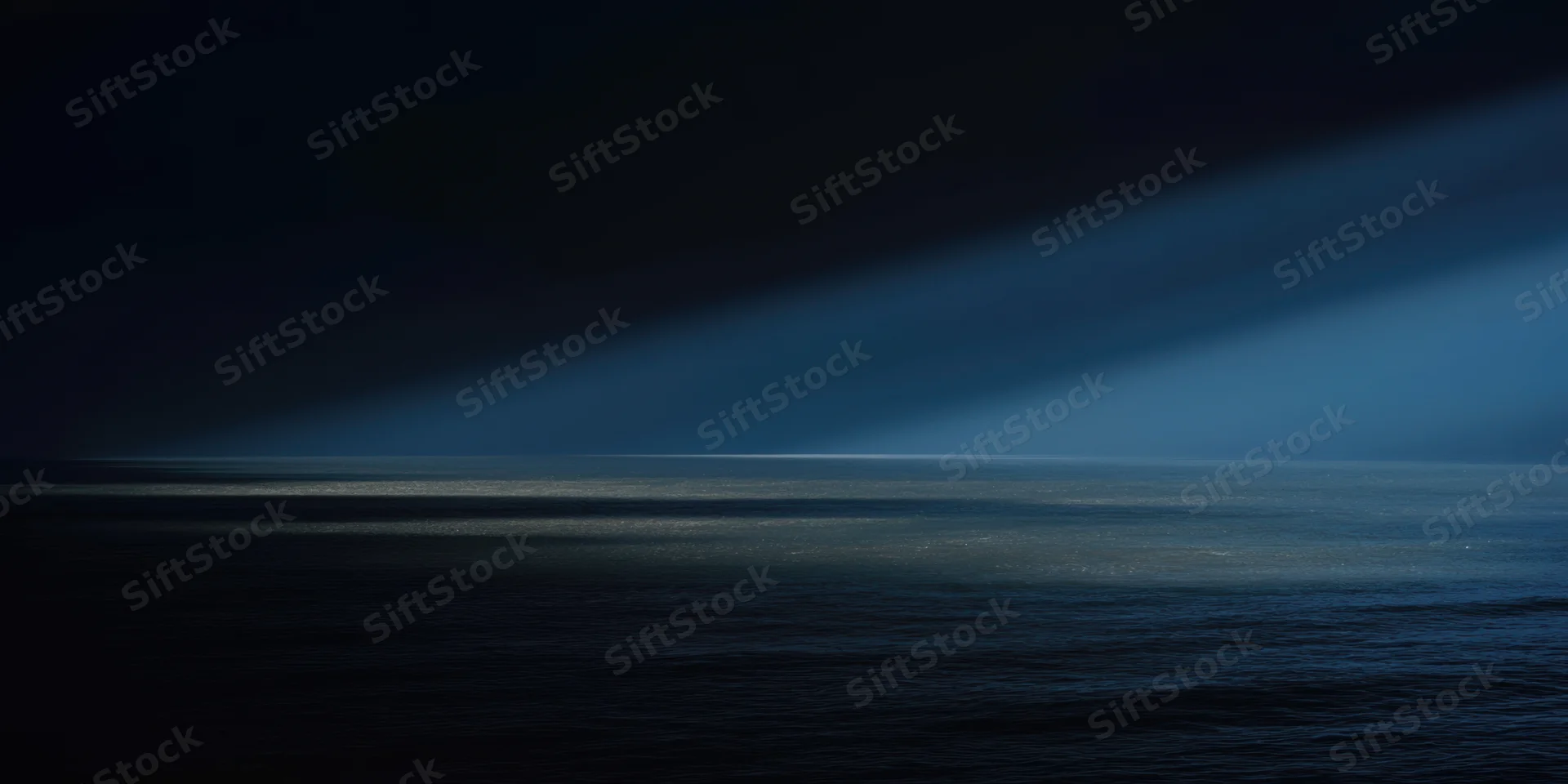 Diagonal beam of light across dark ocean at night