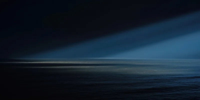Diagonal beam of light across dark ocean at night