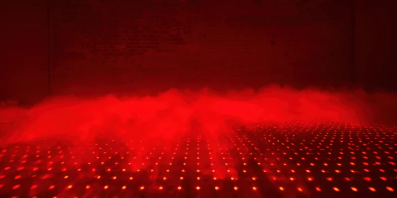 Red fog rolling over a grid of glowing dots on a dark floor in a dimly lit room
