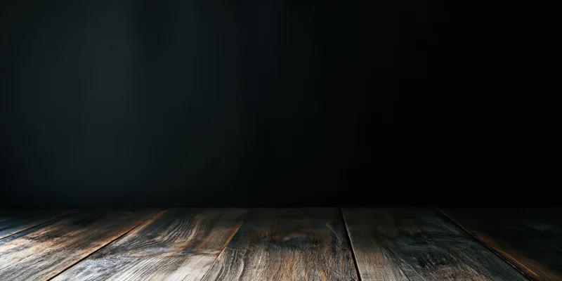 Dark studio interior with wooden floor and black wall fading into shadow, providing copyspace for product display