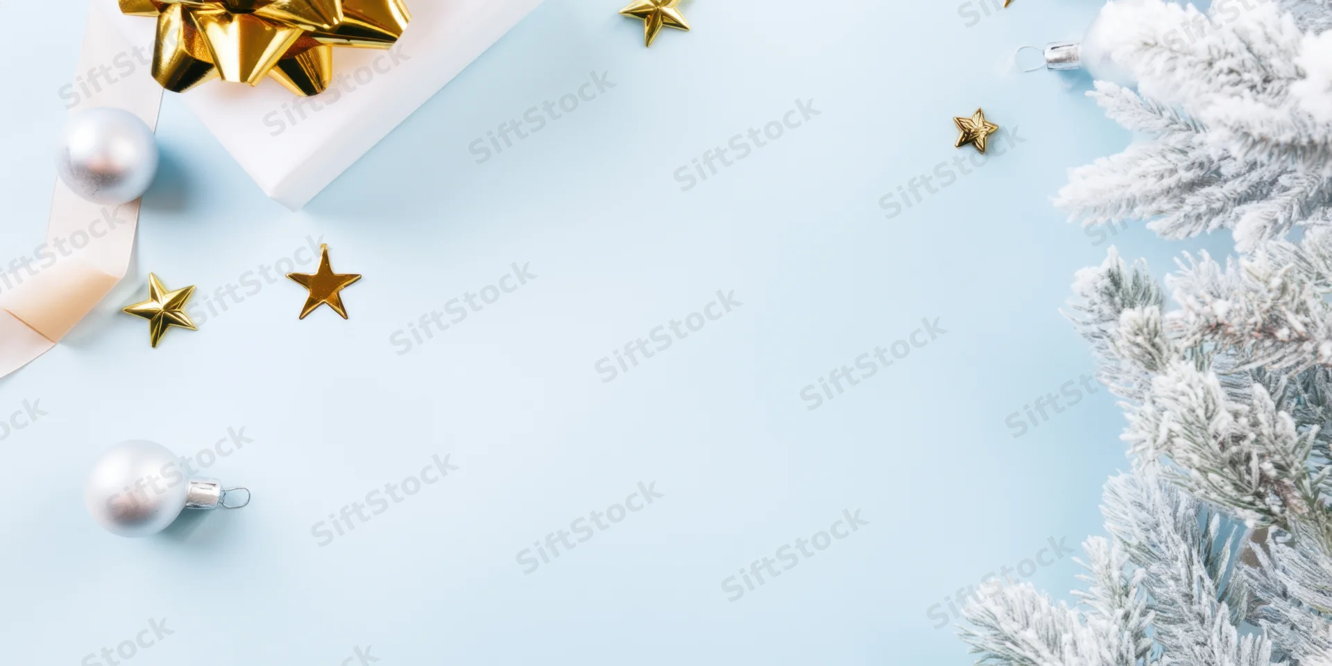 White gift box with gold bow and silver ornaments arranged on pale blue background with snowy pine branches and scattered stars