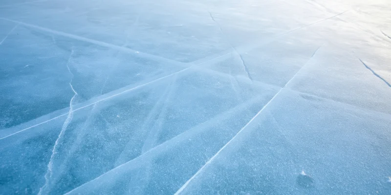 Pale blue ice surface with intersecting cracks forming a network pattern