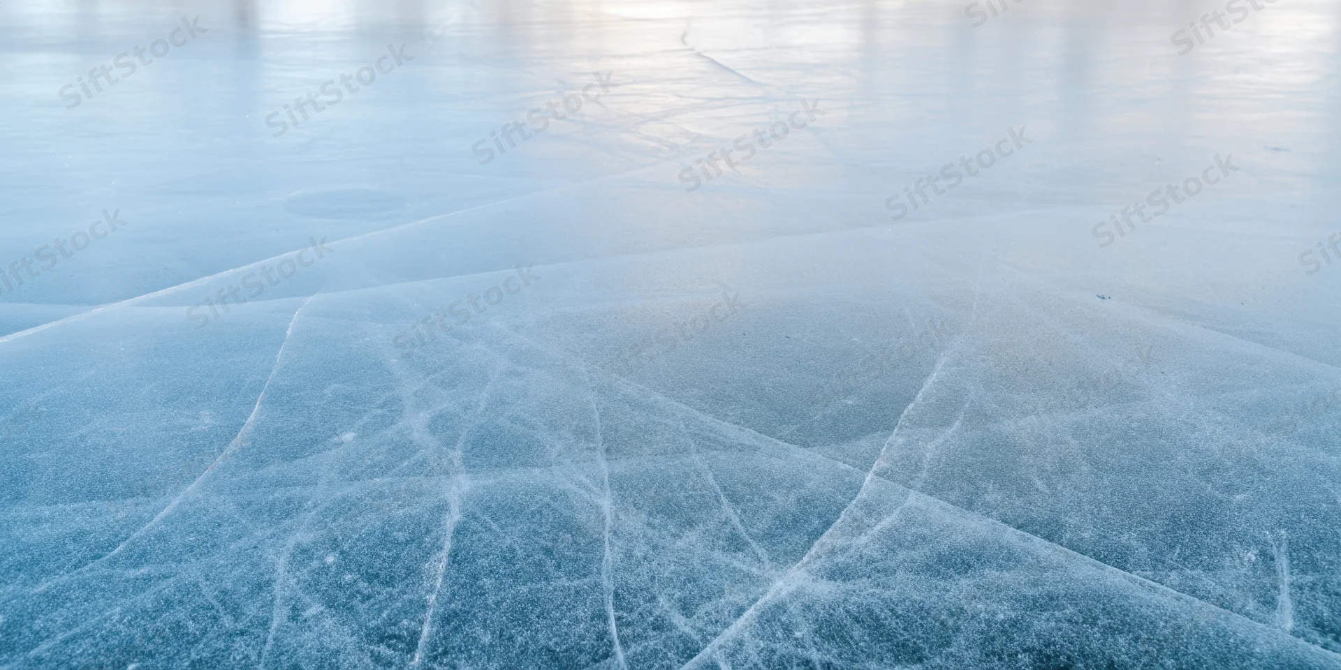 Pale blue ice surface with intersecting cracks and frost patterns