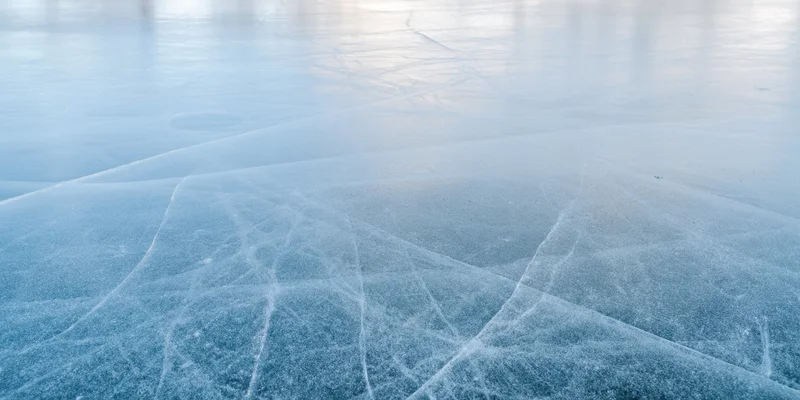 Pale blue ice surface with intersecting cracks and frost patterns