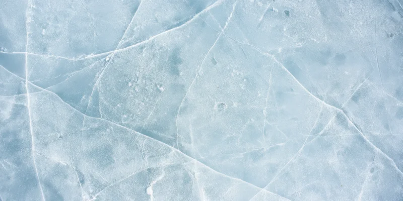 Pale blue ice surface with intersecting cracks and frost patterns