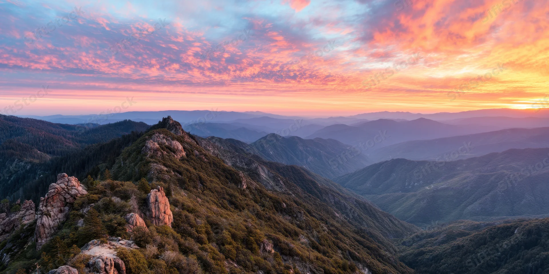Panoramic sunrise over rugged forested mountains and rocky peaks in a layered valley landscape